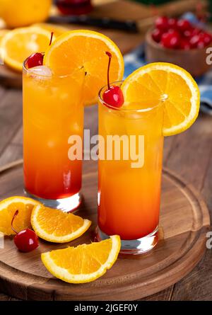 Cocktail tequila all'alba con fetta d'arancia e ciliegia su un rustico tavolo in legno Foto Stock