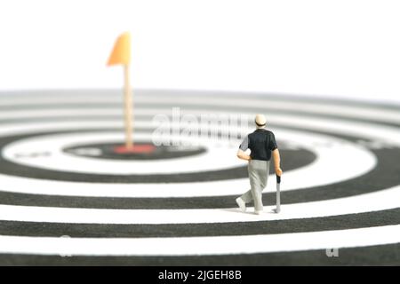 Fotografia di personaggi giocattolo in miniatura. Un golfista uomo in piedi sopra la tavola da disegno con bandiera al centro, isolato su sfondo bianco. Foto immagine Foto Stock