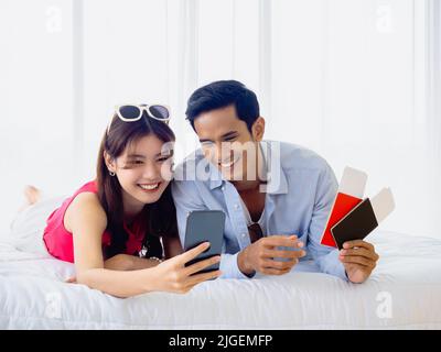 Felice coppia asiatica con prenotazione di volo per il viaggio estivo, viaggi all'estero. Giovane uomo e donna in casual tenendo e guardando lo schermo dello smartphone e tenere Foto Stock