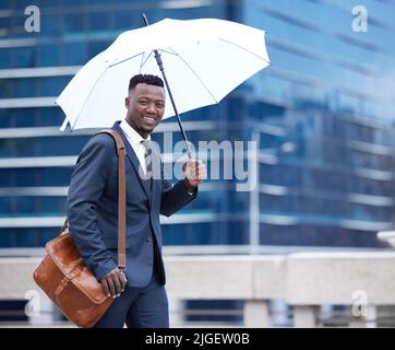 Im preparato per qualsiasi tempo. Un giovane uomo d'affari che tiene un ombrello sotto la pioggia contro uno sfondo di città. Foto Stock