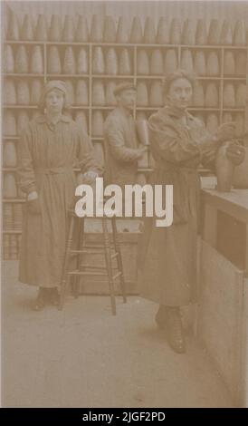 I lavoratori delle munizioni della prima guerra mondiale in una fabbrica britannica. Fotografia di due donne e di un uomo sul lavoro, file di conchiglie sono allineate su scaffali sullo sfondo Foto Stock