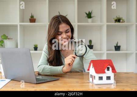 Donna felice mano tenendo lente d'ingrandimento e guardando il modello della casa, la selezione della casa, concetto immobiliare. Foto Stock