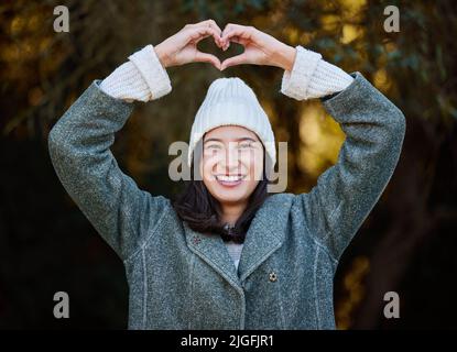 Questa è la mia stagione preferita: Una giovane donna attraente in piedi da sola fuori e facendo un gesto a forma di cuore. Foto Stock