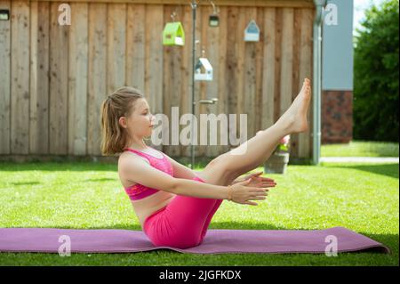 Ragazza felice sportiva adolescente che pratica pilates su tappeto yoga su erba a cortile Foto Stock