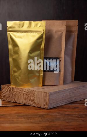 Buste in carta e alluminio con chicchi di caffè e foglie di tè su sfondo di legno scuro. Confezionamento per alimenti e merci mockup marca, shopping offerta, vendita Foto Stock