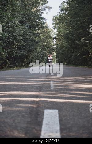 Una giovane coppia felice guida una moto su una strada asfaltata nella foresta, la libertà e la velocità Foto Stock