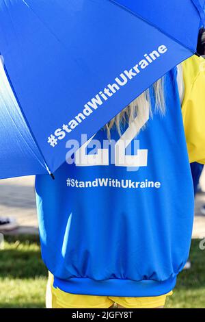 Una giovane ragazza bionda che si prende cura di un ombrello e indossa i colori dell'Ucraina in una manifestazione di pace a Calgary Alberta Foto Stock