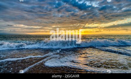 Un'onda dell'oceano sta rompendo contro Un cielo colorato del tramonto Foto Stock