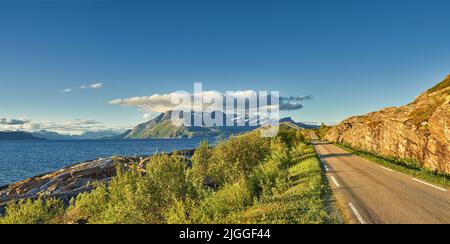 Vista su una strada e vegetazione verde che conduce ad un'idilliaca zona appartata in estate. Grandi alberi verdi che circondano una strada vuota sulla campagna Foto Stock