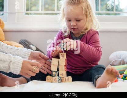 Puntando per un grattacielo. Una bambina accatastando blocchi con sua madre a casa. Foto Stock