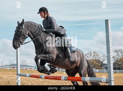 Galoppando via in una nuova avventura. Un giovane cavaliere che salta sopra un ostacolo sul suo cavallo. Foto Stock