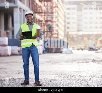Il relativo tutto va secondo il programma. Ritratto a tutta lunghezza di un bel giovane operaio di costruzione in piedi con disegni e appunti su un edificio Foto Stock
