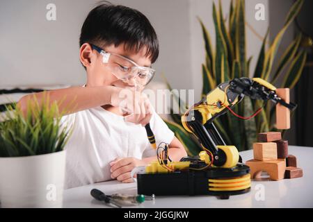 Bambino imparando riparare ottenendo il braccio robot di controllo della lezione, ragazzo piccolo asiatico felice usando il cacciavite per fissare le viti braccio della macchina robotica in casa WO Foto Stock