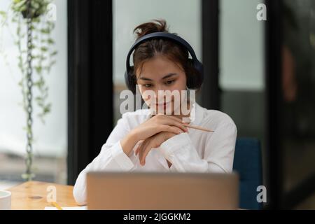 Donna che si concentra sui webinar in classe online. Lo studente indossa le cuffie per ascoltare la lezione online. Foto Stock