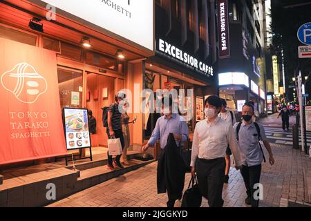 I pedoni che indossano le maschere facciali camminano lungo la strada vicino alla stazione di Shibuya durante il tramonto. Il 30 giugno 2022 il ministro giapponese della Sanità, del lavoro e del benessere Shigeyuki Goto ha annunciato la posizione rivista del governo in materia di maschera: "Anche se si passa da altre persone all'aperto, ad esempio mentre si cammina per lavorare, non è necessario indossare una maschera per il viso fintanto che non ci sono conversazioni o meno." Fondamentalmente dire che indossare una maschera al di fuori non è più consigliato. Foto Stock