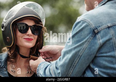 Felice sorridente donna matura lasciando ragazzo per aiutarla con la presa sul casco moto Foto Stock