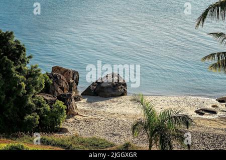 Si affaccia su una piccola spiaggia con palme e grandi rocce tra la sabbia sul bordo delle acque. Giorno tropicale estivo. Foto Stock