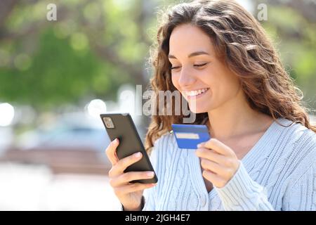 Donna felice che acquista online con carta di credito e telefono cellulare per strada Foto Stock