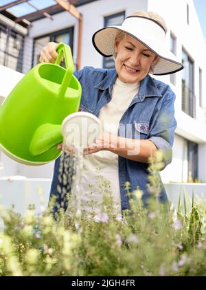 Anche le piante hanno bisogno di un po' di amore. Una donna anziana che fa giardinaggio nel cortile di casa. Foto Stock