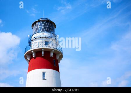 Faro contro il cielo blu. Faro bianco-rosso di giorno in condizioni di sole chiaro Foto Stock