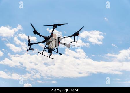 Un drone irroratrice vola su un campo di grano, nel cielo blu con le nuvole. Agricoltura intelligente e coltivazione di precisione. Un drone industriale nel cielo. Foto Stock