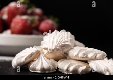 Meringa primo piano e fragole in un piatto su sfondo nero. Dolci alla frutta. Foto Stock