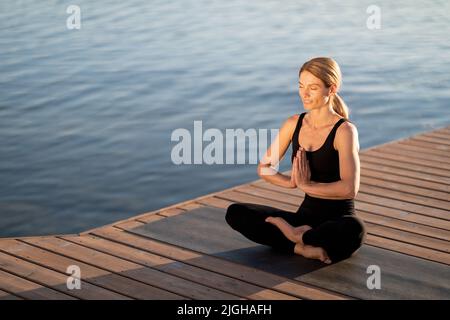 Meditazione del mattino. Calma Donna di mezza età meditating all'aperto su Molo di legno Foto Stock