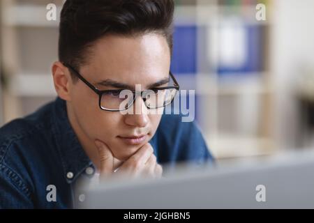 Ritratto di giovane bel ragazzo in occhiali guardando lo schermo del computer Foto Stock