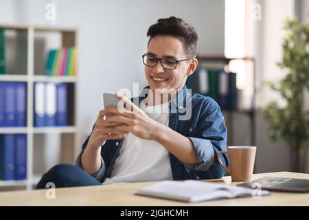 Nuova app. Sorridente giovane uomo d'affari che si rilassa con il laptop sul posto di lavoro in ufficio Foto Stock