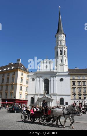 Vienna, Austria - 25 aprile 2012: Chiesa di San Michele (Michaelerkirche) e turisti nella carrozza trainata da cavalli davanti ad essa Foto Stock