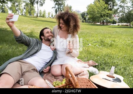 giovane coppia gioiosa che prende selfie su smartphone durante il picnic estivo nel parco Foto Stock