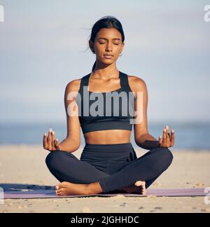 Trovando il suo centro. Scatto a tutta lunghezza di una giovane donna attraente meditando sulla spiaggia. Foto Stock