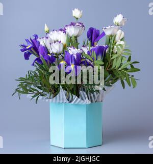 Bouquet luminoso originale con eustoma bianco, tulipani, iridi viola e ciuffi di verde. Bouquet di eustoma in una confezione regalo di cartone turchese su un bl Foto Stock