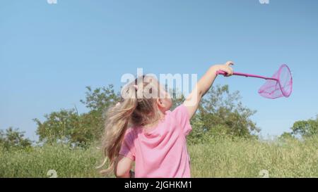 La bambina cattura le bolle di sapone in rete farfalla mentre gioca in erba alta nel parco. Carino ragazza sorride e cattura su bolle di sapone in aereo i Foto Stock