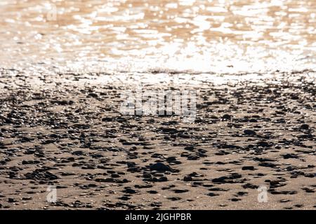 Spiaggia ciottoli e schiuma di mare in contrasto luce pomeriggio su una spiaggia di Ayia Eirini a Cipro. Adatto come sfondo Foto Stock