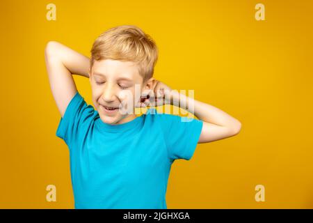 Un ragazzo su sfondo giallo vestito con una T-shirt blu si allunga e chiude gli occhi Foto Stock