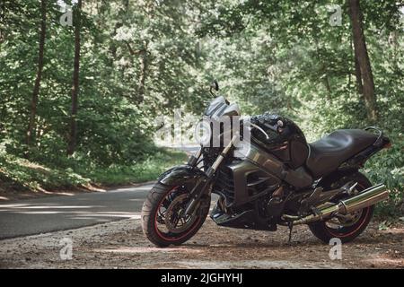 Bici da strada nera nella foresta sul lato strada della strada asfaltata, nessuna gente Foto Stock