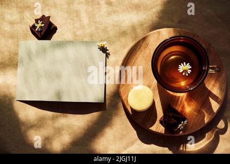 Tempo estetico del tè estivo, tè alle erbe e dessert di macaron all'esterno nella terrazza sotto le ombre dure alla moda. Mock up di carta di cancelleria per il desiderio, il saluto, gli inviti o la ricetta Foto Stock