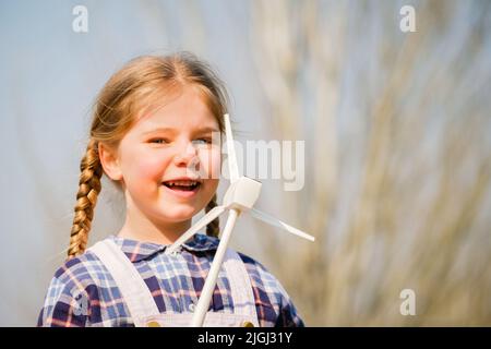 Il bambino gioca e guarda interessato a un giocattolo a turbina eolica - concetto di generazione futura e Enewable Energy Foto Stock