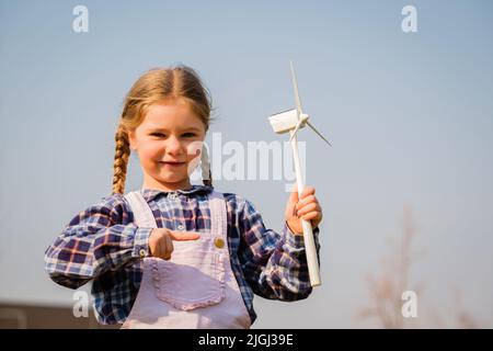 Il bambino gioca e guarda interessato a un giocattolo a turbina eolica - concetto di generazione futura e Enewable Energy Foto Stock