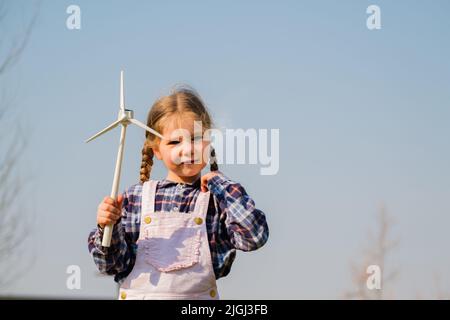 Il bambino gioca e guarda interessato a un giocattolo a turbina eolica - concetto di generazione futura e Enewable Energy Foto Stock