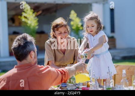 Famiglia multi generazione che ha festa del giardino, la bambina sta versando il succo al suo padre. Foto Stock