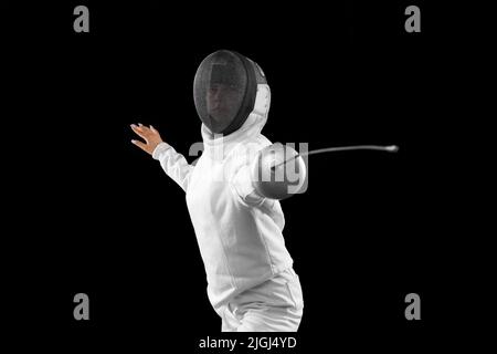 Fencer femminile energico in costume bianco e maschera in azione, movimento isolato su sfondo scuro. Sport, gioventù, attività, abilità, realizzazioni Foto Stock