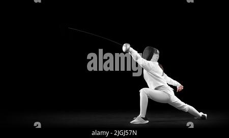 Fencer femminile energico in costume bianco e maschera in azione, movimento isolato su sfondo scuro. Sport, gioventù, attività, abilità, realizzazioni Foto Stock