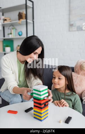 felice babysitter giocare a blocchi di legno gioco con ragazza felice in soggiorno Foto Stock