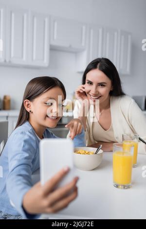 la ragazza felice che mostra il telefono mobile offuscato al babysitter durante la colazione Foto Stock