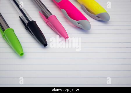 Primo piano di penne colorate e evidenziatori fluorescenti appoggiati su un foglio di carta rigato. Sfondo con messa a fuoco selettiva e spazio vuoto per il testo Foto Stock