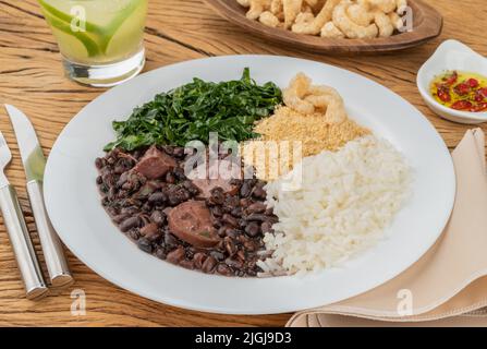 Tipica feijoada brasiliana con riso, pepe, farofa, kale, caipirinha e crackling. Foto Stock