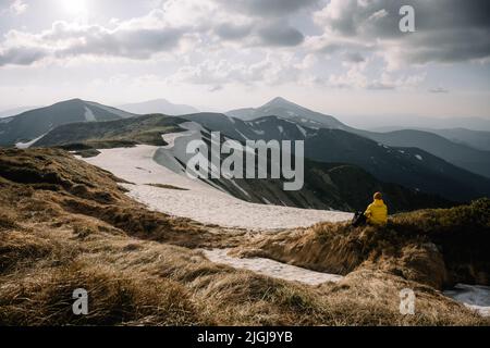 Un turista siede sul bordo di una cima di montagna. Montagne nebbia sullo sfondo. Fotografia di paesaggio Foto Stock