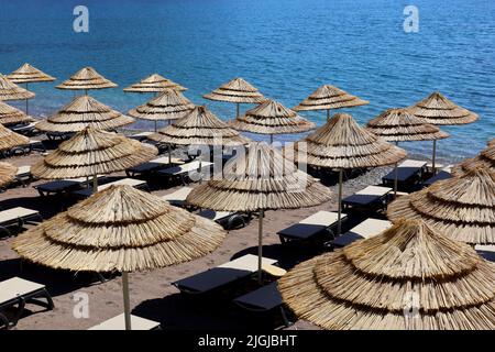 Spiaggia di ciottoli vuota con ombrelloni in vimini e sedie a sdraio. Pittoresca vista sul mare con acqua azzurra, località estiva Foto Stock